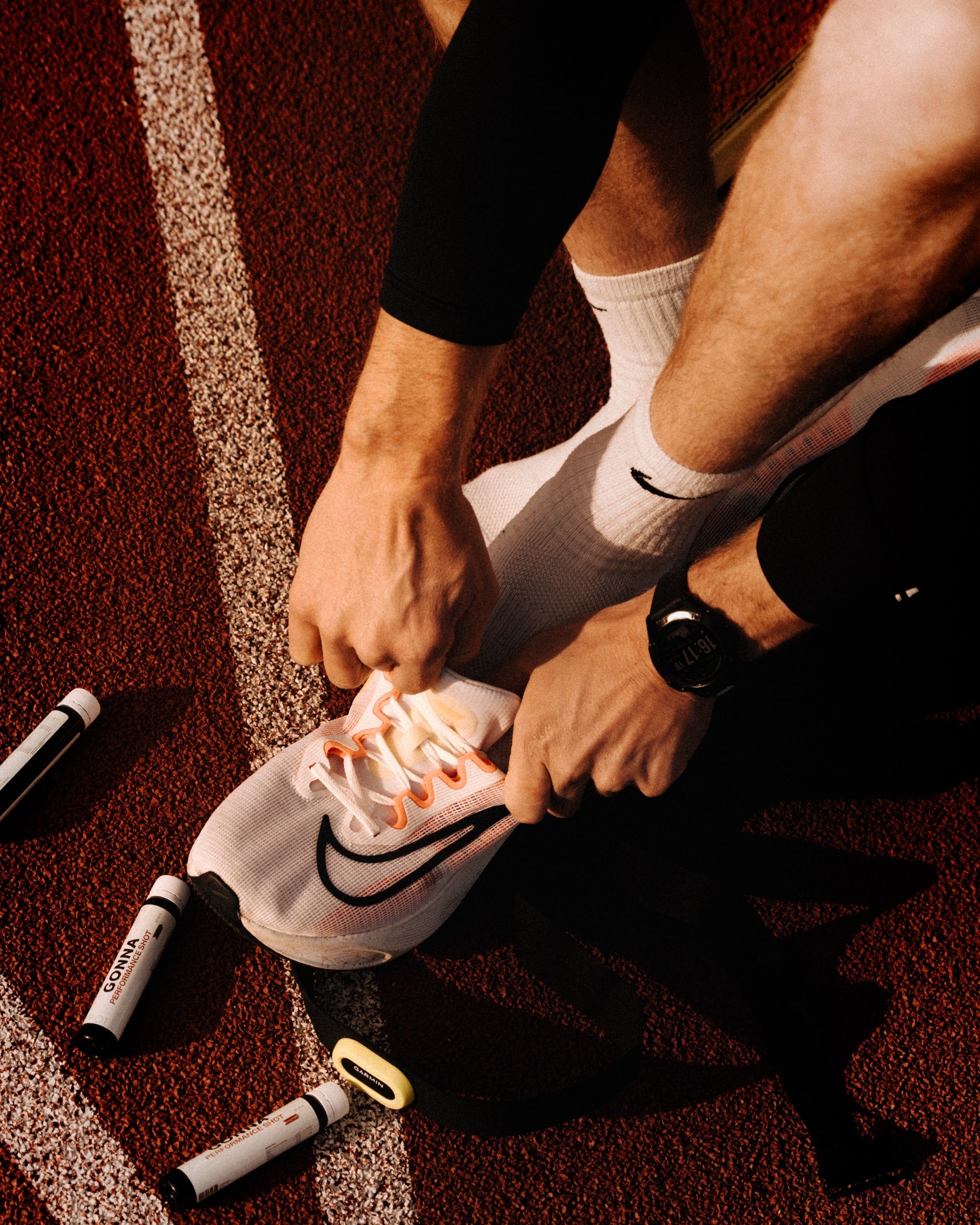 Runner lacing spikes on the track beside GONNA fuel